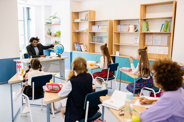 Teacher engaging students with a globe in a diverse classroom setting for interactive learning.